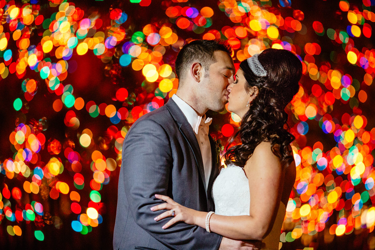 bride and groom kissing at night in front of christmas tree lights