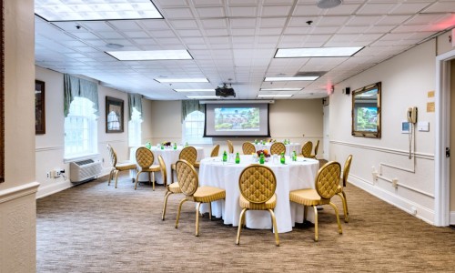 banquet room with three tables set with chairs and projector