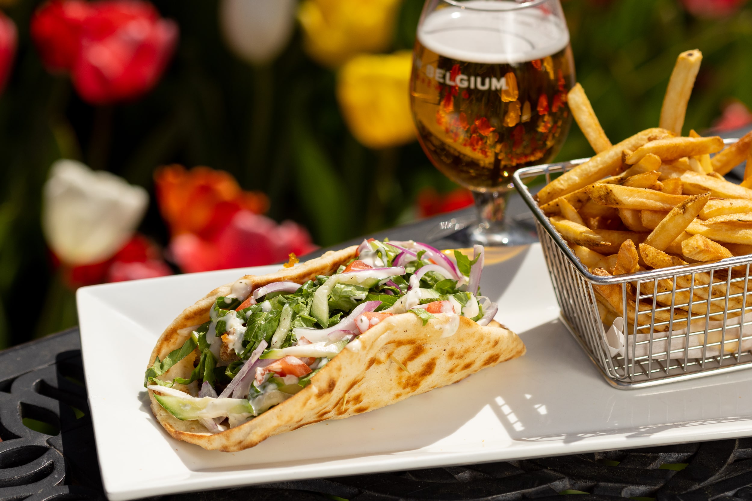 pita, fries in a basket and glass of beer on a plate outside on a table