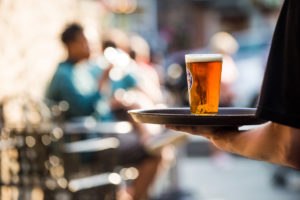 server holding one pint glass of beer on serving tray