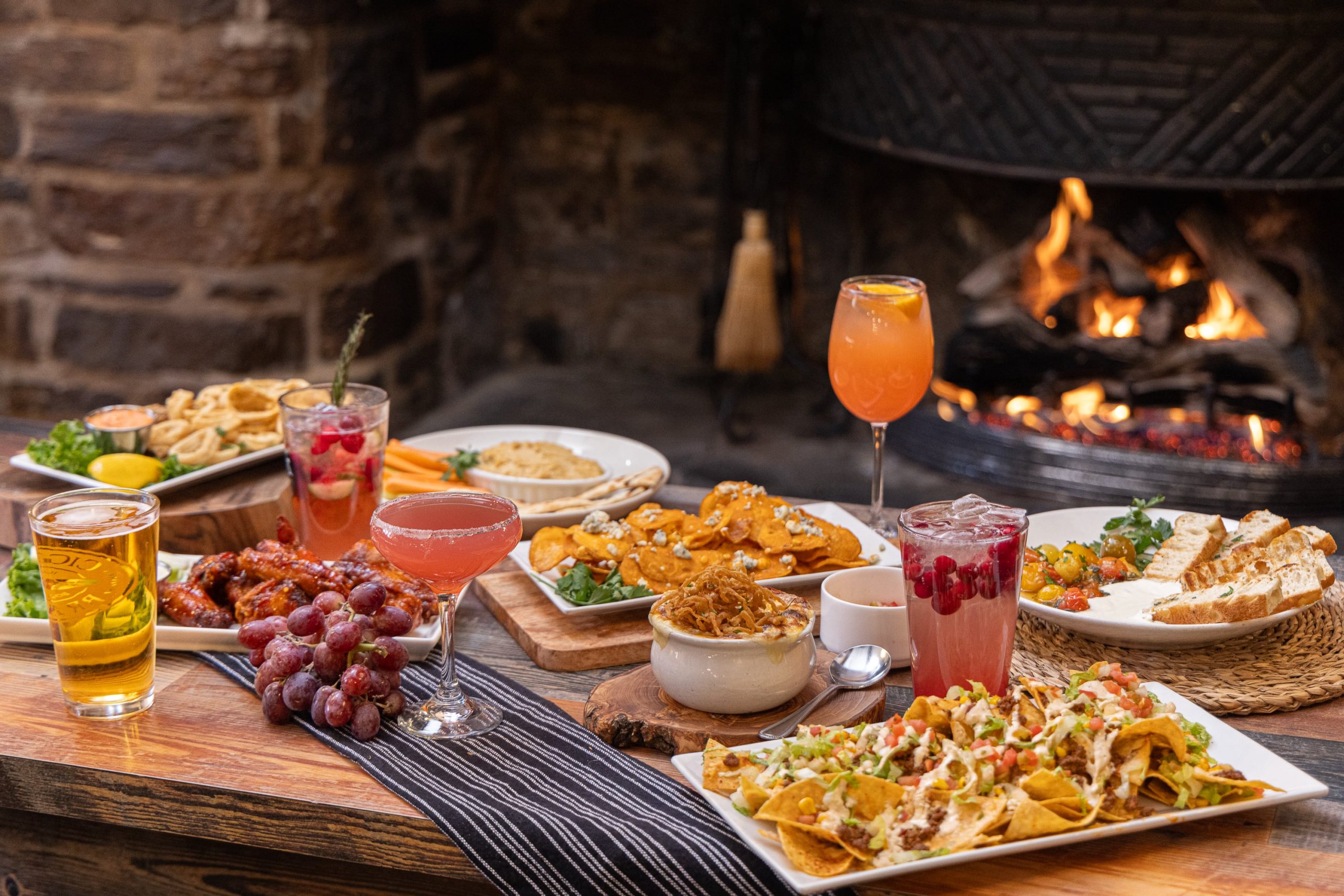 food and drink on table with lit fireplace in the background