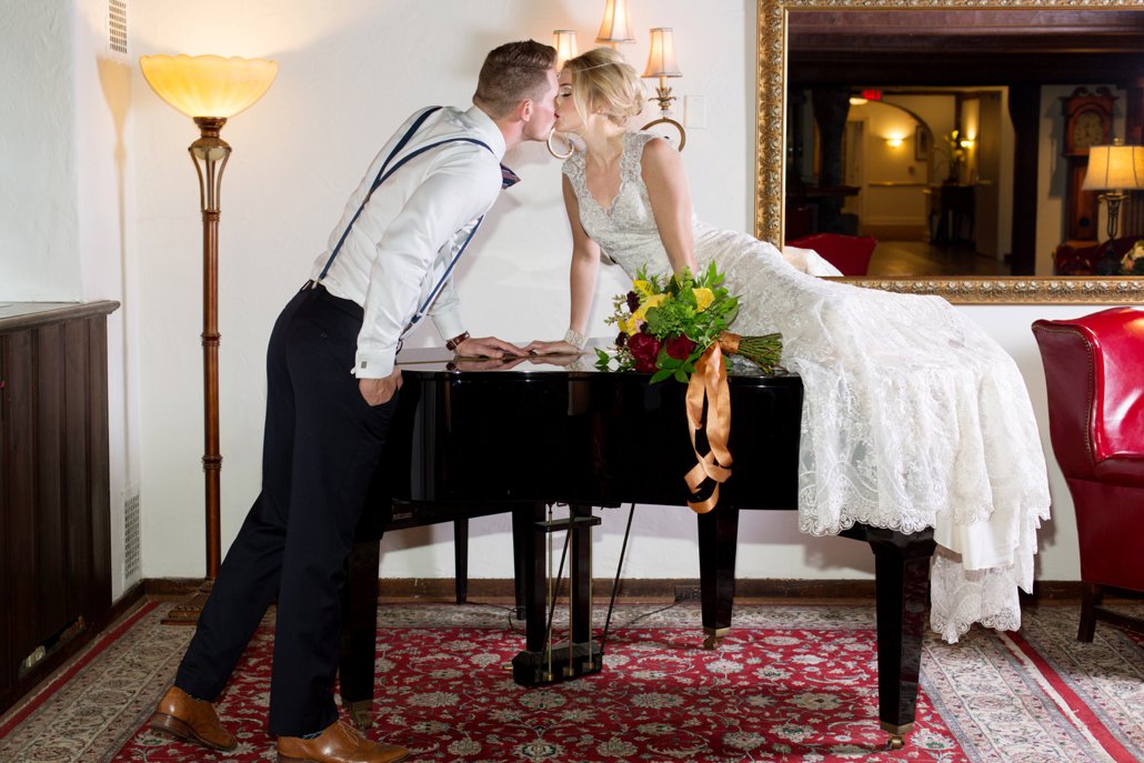 bride on top of piano leaning over to kiss groom